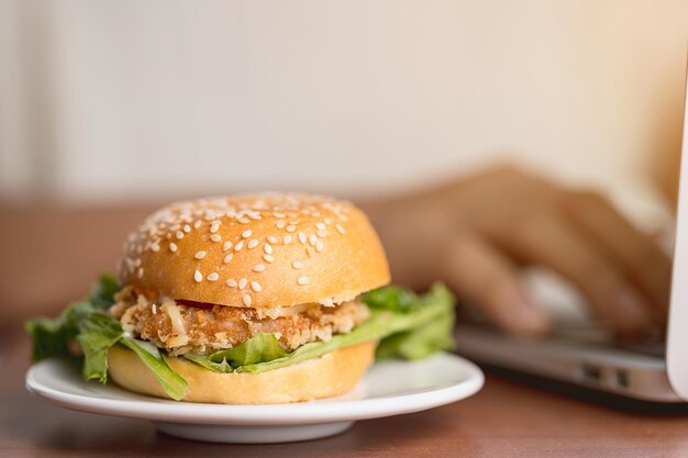 Foto ein köstlicher hamburger auf dem tisch, während man am laptop arbeitet