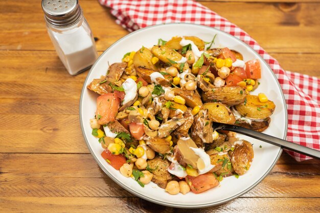 Ein köstlicher Kartoffel-Kichererbsen-Tomaten- und Pilzsalat mit Petersilie und Aioli in einer Schüssel mit Gabel und Löffel auf einem Holztisch Gesundes hausgemachtes veganes Essen