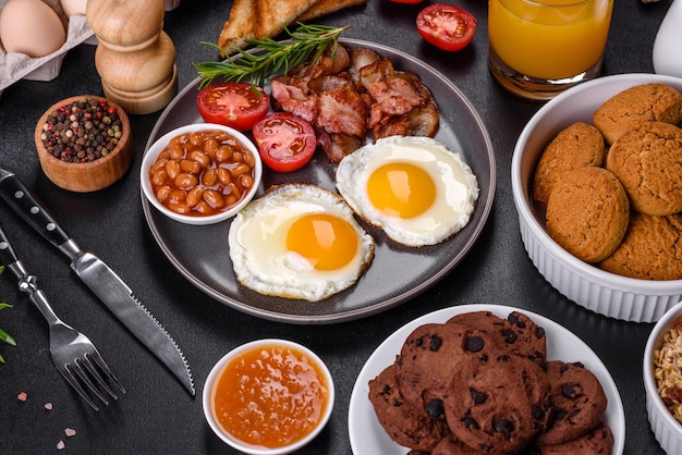 Ein köstliches, nahrhaftes, gesundes Frühstück mit Spiegeleiern, Speckbohnen, einem Glas Saft, Haferplätzchen, Milch und Marmelade. Gesunde Ernährung am Anfang des Tages