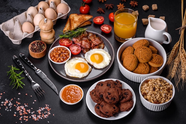 Ein köstliches, nahrhaftes, gesundes Frühstück mit Spiegeleiern, Speckbohnen, einem Glas Saft, Haferplätzchen, Milch und Marmelade. Gesunde Ernährung am Anfang des Tages