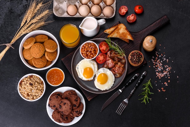 Ein köstliches, nahrhaftes, gesundes Frühstück mit Spiegeleiern, Speckbohnen, einem Glas Saft, Haferplätzchen, Milch und Marmelade. Gesunde Ernährung am Anfang des Tages