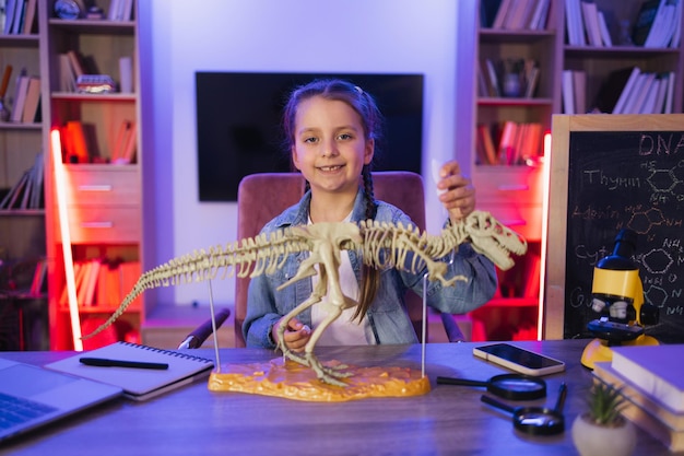 Ein konzentriertes kleines Mädchen studiert fossile prähistorische Tiere am Abend im Wohnzimmer