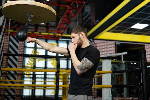 Ein konzeptionelles Porträt eines brutal tätowierten Boxers, der im Ring trainiert und einen Boxsack schlägt