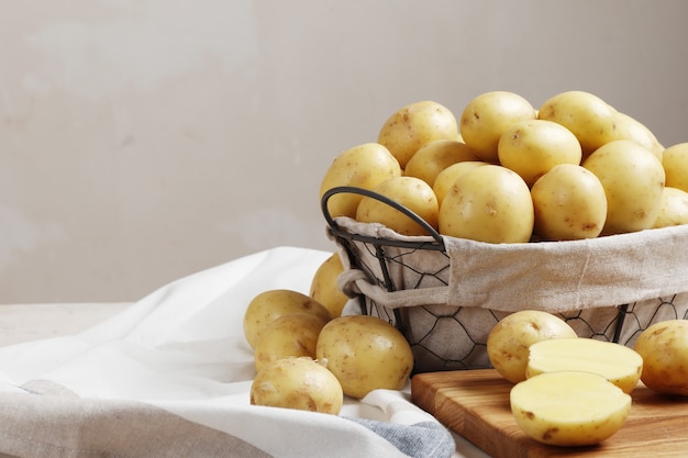 Ein Korb voller frischer, junger Kartoffeln auf einem Holztisch, ein Messer und ein Küchenbrett mit Platz für Text.