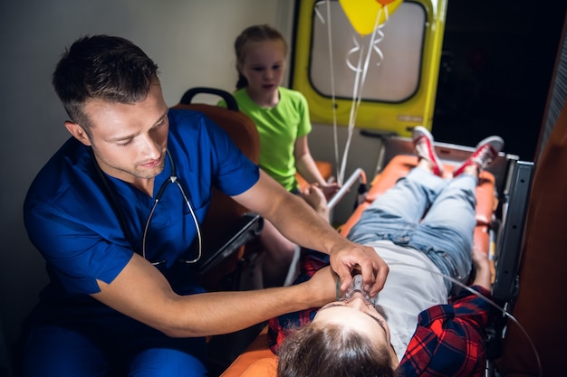 Ein Korpsmann in Uniform, der einer bewusstlosen Frau, die auf einer Trage in einem Krankenwagen liegt, eine Sauerstoffmaske anlegt.