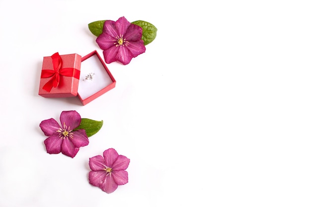 Foto ein kostbarer ring mit einem großen stein in einer roten box mit einer roten schleife mit drei rosa clematisblüten