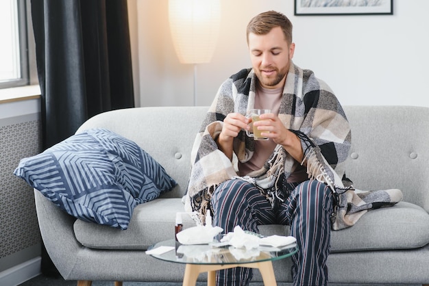 Ein kranker Mann sitzt zu Hause auf einem grauen Sofa mit einer Decke Krankheitsschutz Coronavirus Krankheit Grippe