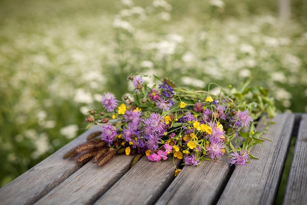 Ein Kranz aus Wildblumen auf einem hölzernen Gartentisch vor dem Hintergrund einer grünen blühenden Wiese