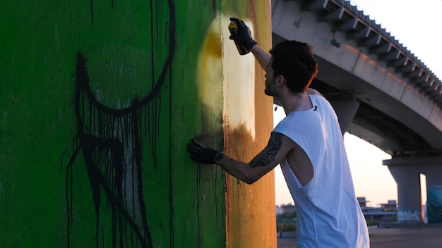 Ein kreativer Mann, der in der Nähe der Wand steht und ein Graffiti mit einer Aerosolfarbe malt