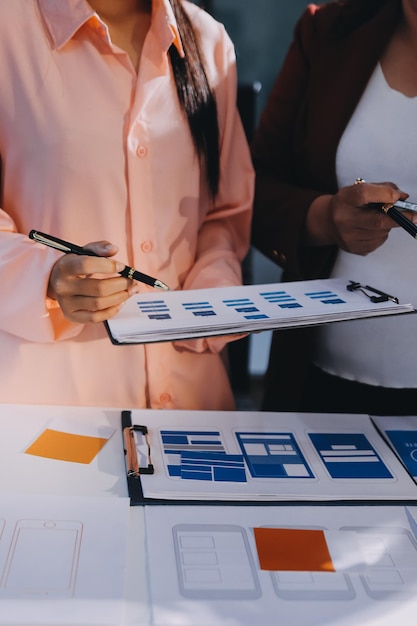 Ein kreatives Team junger asiatischer Geschäftsleute arbeitet zusammen an einem Mobile-App-Software-Design-Projekt, einem Brainstorming-Treffen, einer Internettechnologie, einem Smartphone, einem Web-App-Designer, einem Büro, einem Mitarbeiter, einem Teamwork-Konzept.