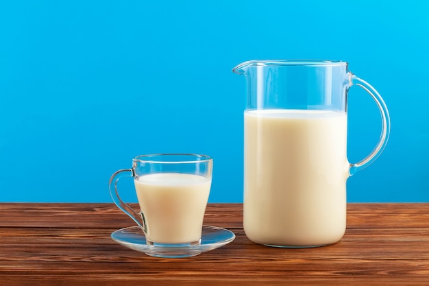 Ein Krug und ein Glas Milch auf Holztisch auf Blau