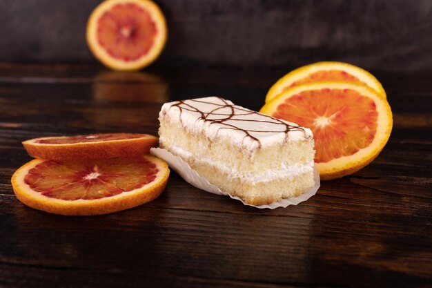 Ein Kuchen mit weißem Zuckerguss und roten Orangen auf dunklem Holzhintergrund.