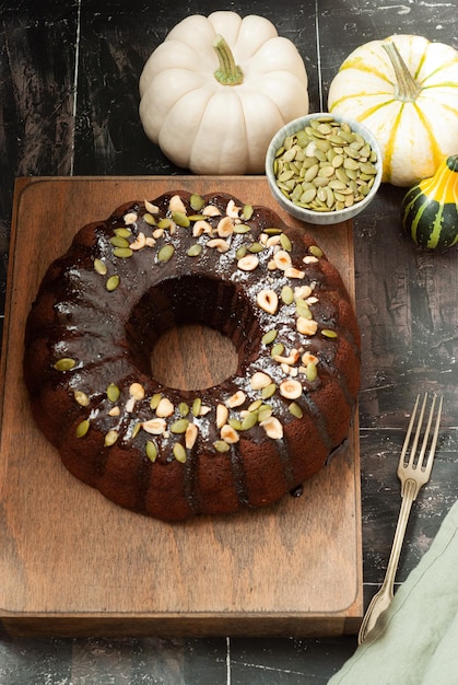 Ein Kürbis-Bundt-Kuchen mit Schokoladenganache und Kürbiskernen auf einem Holzbrett.