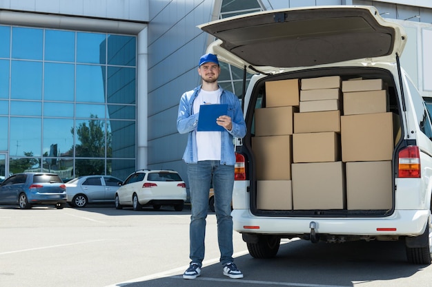 Ein Kurier mit einem Ordner in der Hand neben einem Auto mit Kartons