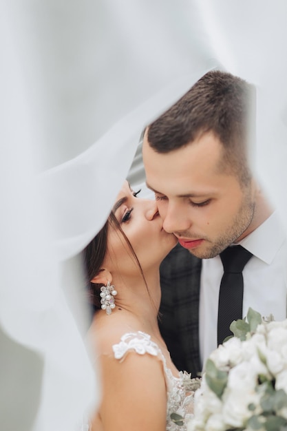 Ein Kuss zwischen Braut und Bräutigam vor einem weißen Vorhang