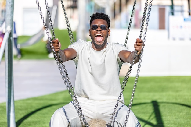 Ein lächelnder afroamerikanischer Mann sitzt auf einer Schaukel in einem Park