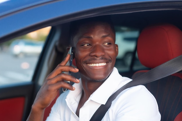 Ein lächelnder afroamerikanischer Mann sitzt mit einem Telefon in der Hand in einem Auto Positive Emotionen