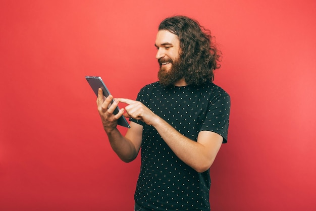Ein lächelnder gutaussehender Mann genießt es, sein neues Tablet zu benutzen, während er darauf scrollt