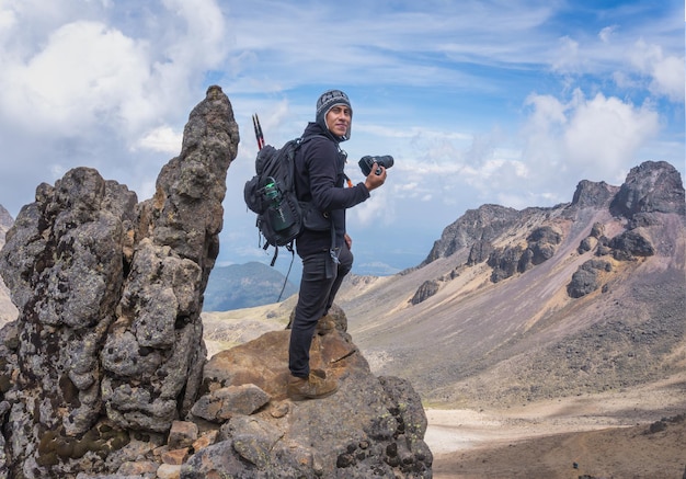 Ein lächelnder hispanischer Wanderer mit einer professionellen Kamera auf einer Kamera auf dem Vulkan Iztaccihuatl