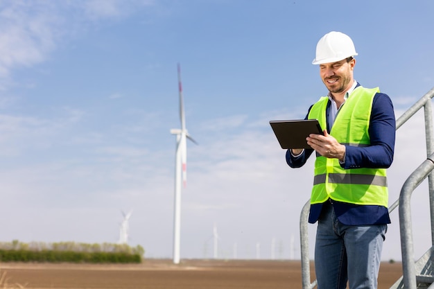 Foto ein lächelnder ingenieur mit tablet inspiziert windturbinen an einem sonnigen tag