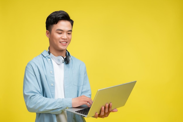Ein lächelnder junger asiatischer Geschäftsmann zeigt einen Laptop auf einem isolierten gelben Hintergrund