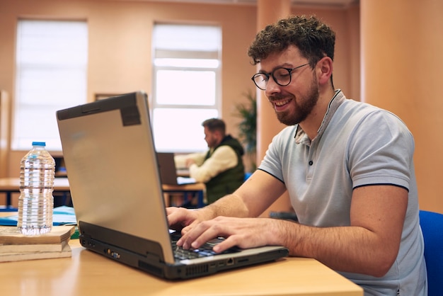 Ein lächelnder junger Mann arbeitet mit seinem Laptop in der Bibliothek