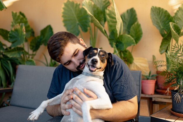 Foto ein lächelnder junger mann hält seinen hund hoch, während er mit seinen pfoten spielt. der hund schaut in die kamera