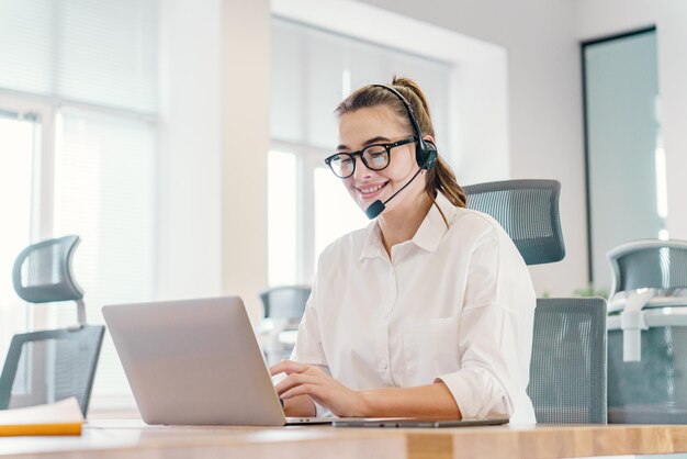 Ein lächelnder Kundendienstmitarbeiter mit Headset arbeitet fleißig an einem Laptop in einem hellen