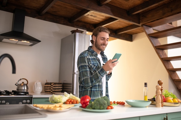 Ein lächelnder Mann, der seiner Freundin beim Kochen eine SMS sendet