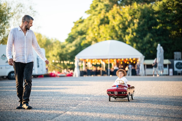 Ein lächelnder Vater fährt ein glückliches Kind in einem roten Spielzeugwagen