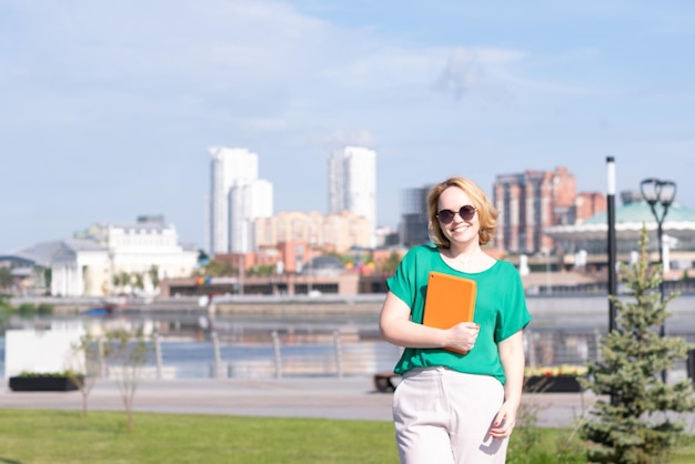 Ein lächelndes Bloggermädchen mit Sonnenbrille, das auf der Straße ein Notizbuch oder Tablet in den Händen hält