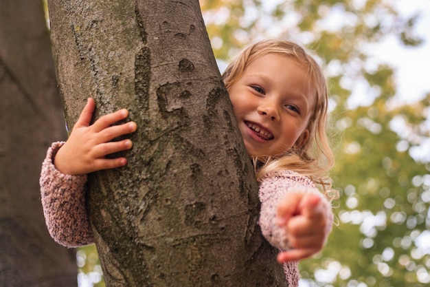 Foto ein lächelndes blondes mädchen zeigt mit dem finger auf ein kind, das auf einem baum liegt