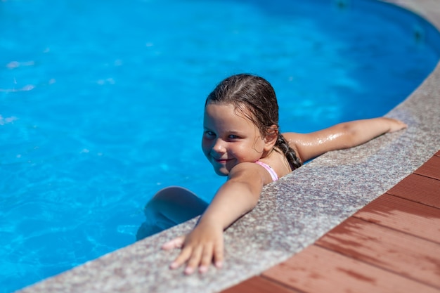 Ein lächelndes fünfjähriges Mädchen legte ihre Hände weit auf den Rand des Pools im Hotel das Konzept eines ...