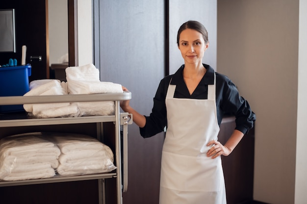 Ein lächelndes Hotelmädchen, das mit einem Reinigungswagen in einem Korridor steht