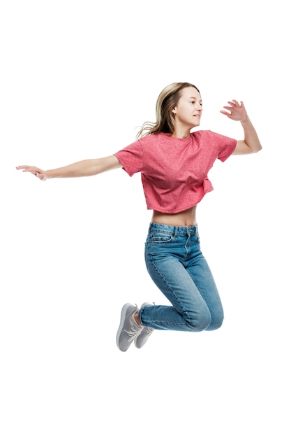 Ein lächelndes junges Mädchen in Jeans und einem roten T-Shirt springt. Positiv und glücklich. Ohren an einer weißen Wand. Vollständige Höhe. Vertikale.