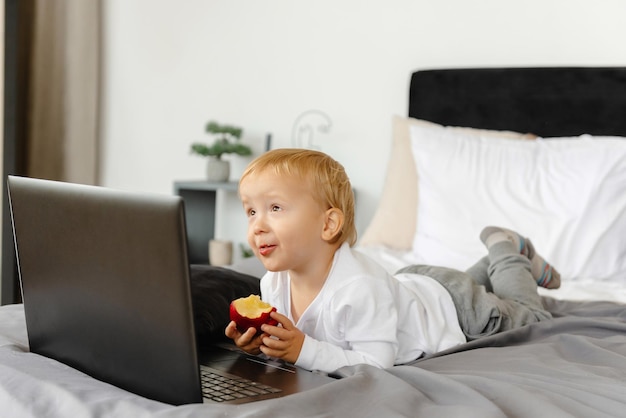 Ein lächelndes Kind, das auf einem Bett neben seinem Laptop liegt