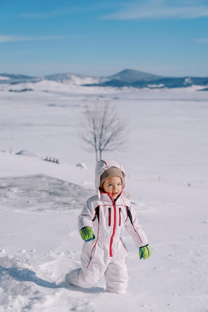 Ein lächelndes kleines Mädchen geht durch tiefe Schneeflächen in einem Bergtal