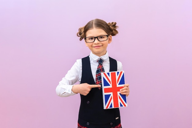 Ein lächelndes Schulmädchen zeigt mit dem Finger auf ein englisches Lehrbuch. ein Student in Gläsern mit einem Buch auf einem lila isolierten Hintergrund.