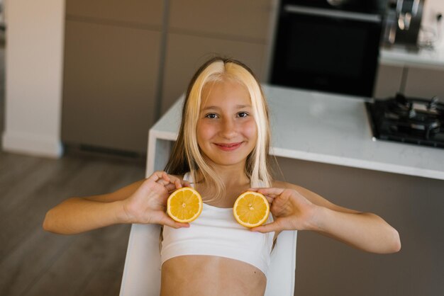 Foto ein lächelndes teenagermädchen schaut in die kamera und bedeckt ihre brust mit halben orangen