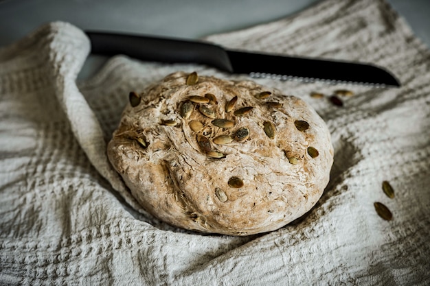 Ein Laib frisches hausgemachtes Vollkornbrot auf einem beigen Handtuch und einem schwarzen Messer