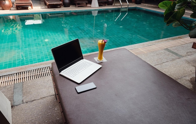 Ein Laptop-Handy und ein Mango-Smoothie auf einer Sonnenbank