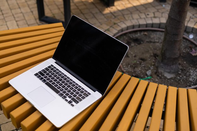 Ein Laptop mit leerem Bildschirm steht auf einer Holzbank im Innenhof, Arbeitsplatz des Freiberuflers im schönen Hausgarten