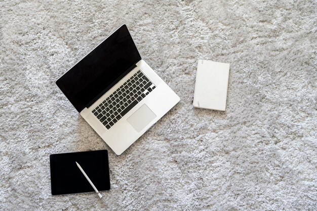 Ein Laptop und andere Geräte auf dem Boden auf dem weichen Teppich im Wohnzimmer zu Hause, Isolation während Coronavirus-Pandemie