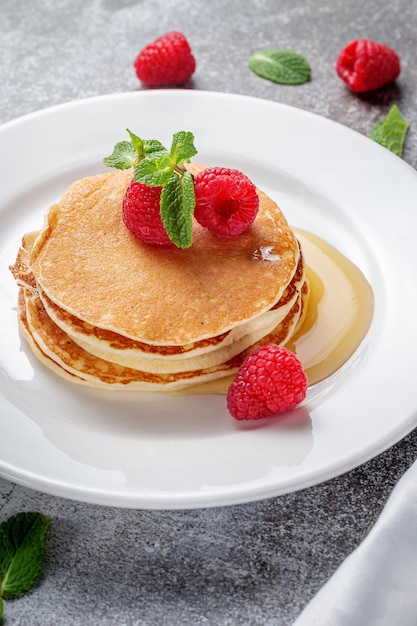 Ein leckeres Frühstück. Süße gebratene Himbeer-Minz-Pfannkuchen in einem weißen Teller mit Sauerrahm auf einem grauen Steintisch mit Serviette und Besteck