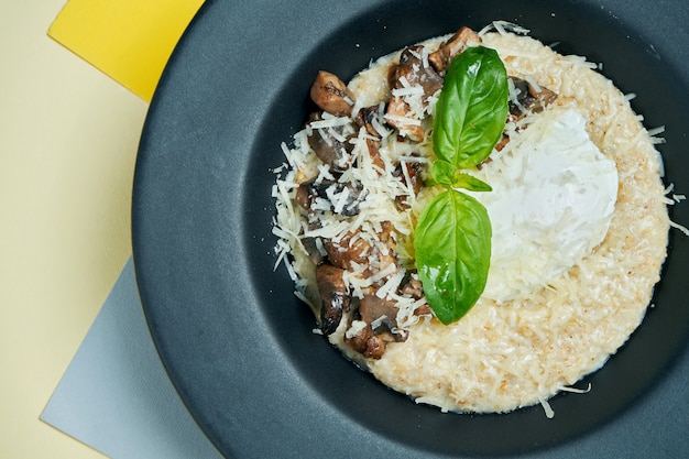 Ein leckeres und gesundes Frühstück. Haferflocken mit pochiertem Ei, Parmesan und Pilzen in einem schwarzen Teller auf s