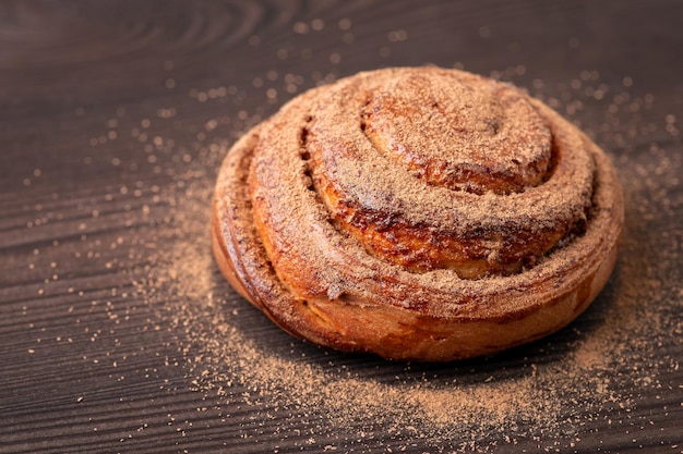 Ein leckeres Zimtbrötchen auf Holztisch, gewürzt mit gemahlenem Zimt. Kochen zu Hause