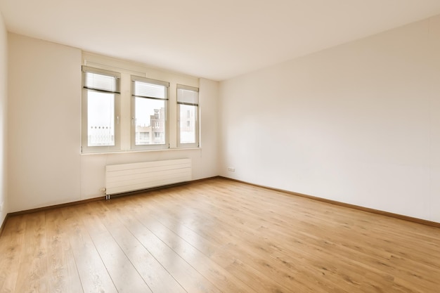 Foto ein leerer raum mit holzboden und weißer farbe an den wänden. in der ecke befindet sich ein großes fenster