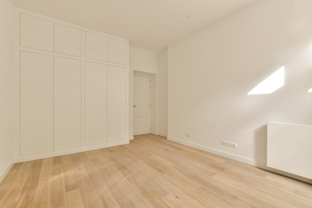 Ein leerer Raum mit Holzböden und weißen Schränken an der Wand rechts, dort gibt es keine Tür