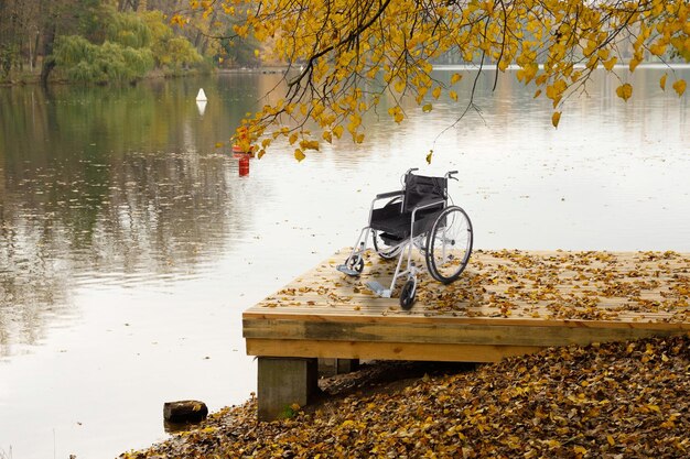 Ein leerer Rollstuhl auf einer Holzbrücke in der Nähe des Flusses im Herbstpark Das Konzept der Zugänglichkeit von Menschen mit Behinderungen Foto in hoher Qualität