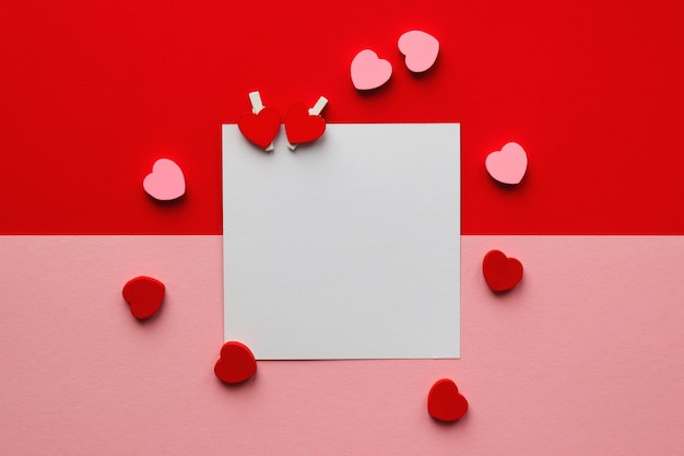 Ein leeres Blatt Papier, umgeben von Herzen auf einem Rot-Rosa